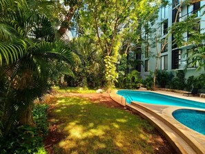 A swimming pool surrounded by lush greenery and a modern building. - Quiet 2BR Haven with Worspace Surrounded by Nature (Playa del Carmen)