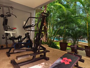 A gym with exercise equipment, a bench, and a view of a pool and greenery. - Quiet 2BR Haven with Worspace Surrounded by Nature (Playa del Carmen)