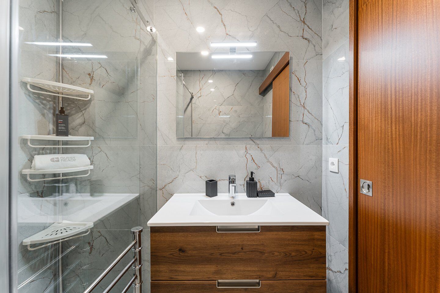 A modern bathroom with a marble backsplash, a glass shower enclosure, a wooden vanity with a sink, and a mirror above the vanity.