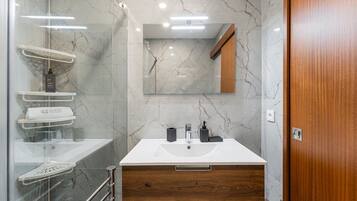 A modern bathroom with a marble backsplash, a glass shower enclosure, a wooden vanity with a sink, and a mirror above the vanity.