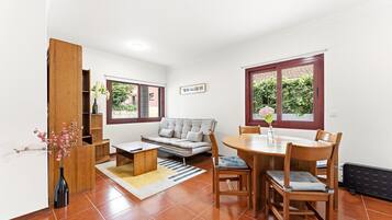 A compact living space with a sofa, dining table, chairs, a small coffee table, and a bookshelf.