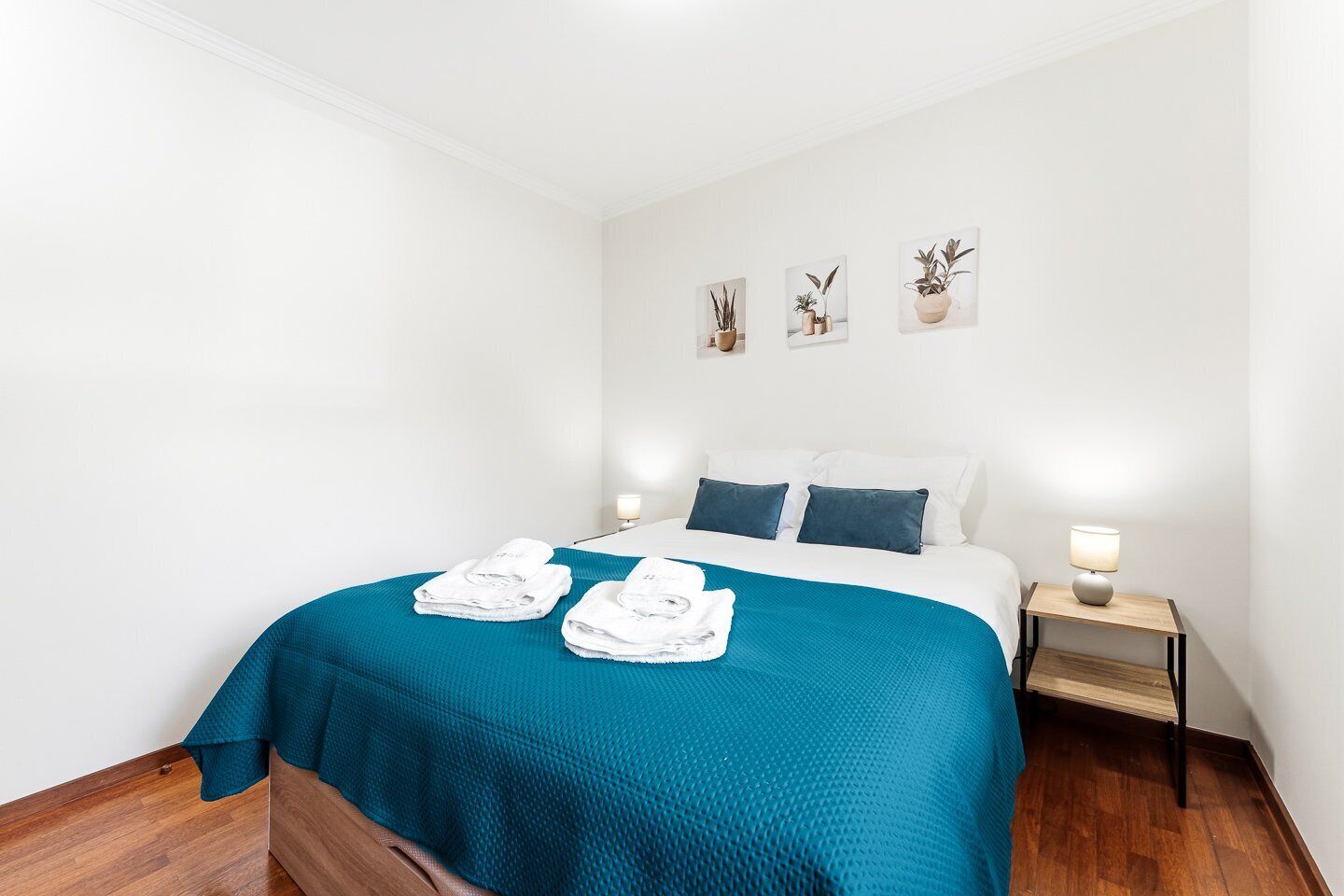 A hotel room with a bed, two bedside lamps, a blue bedspread, and a set of white towels.