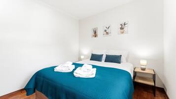 A hotel room with a bed, two bedside lamps, a blue bedspread, and a set of white towels.