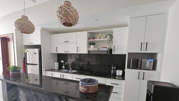 A modern kitchen with white cabinets, a black countertop, and two pendant lights. - Eden Tropical new 1BR Condo, Walk to Beach ,pool (Punta Cana)