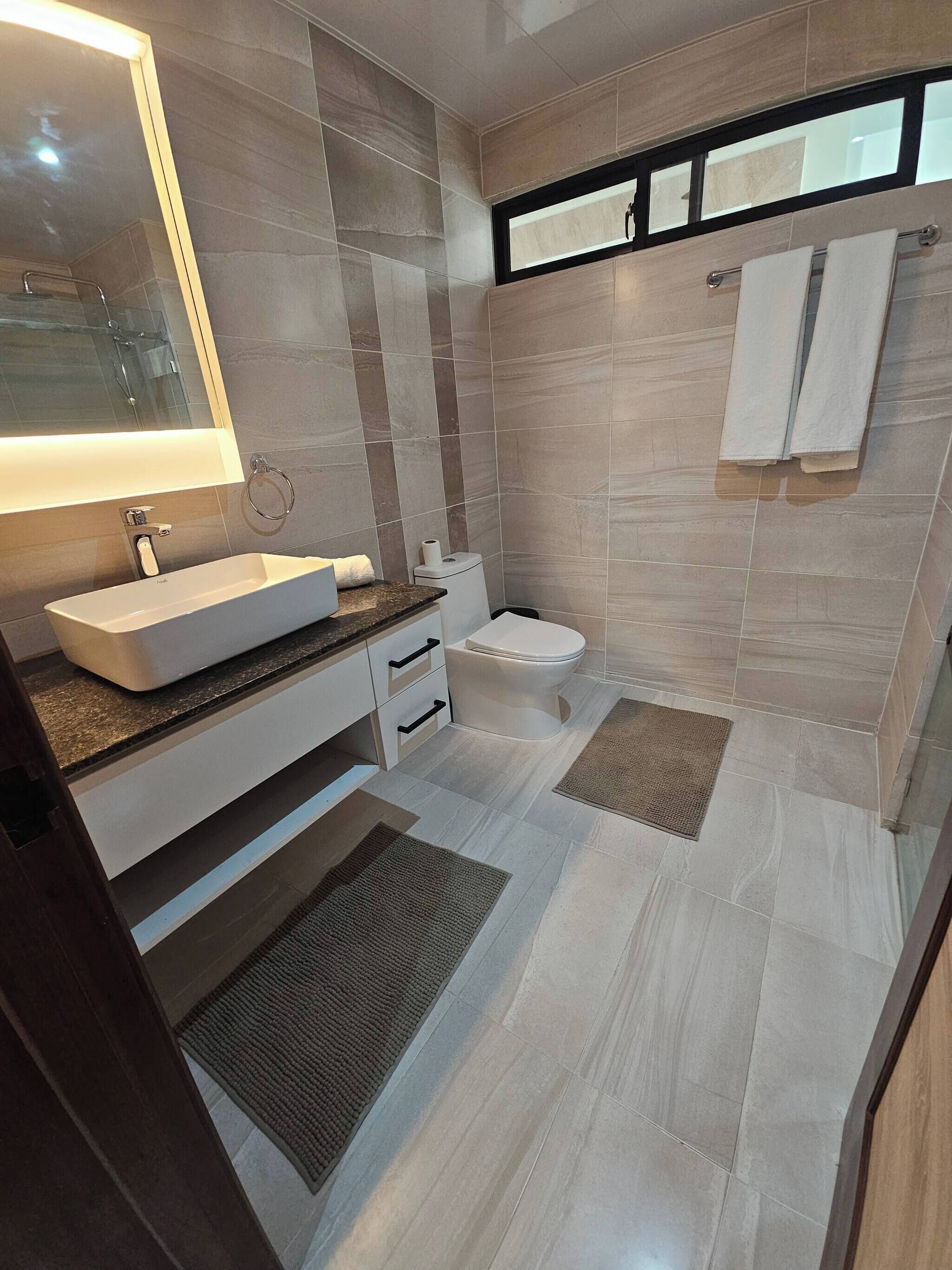 Une salle de bain moderne avec un grand miroir, un lavabo, des toilettes et un espace douche.