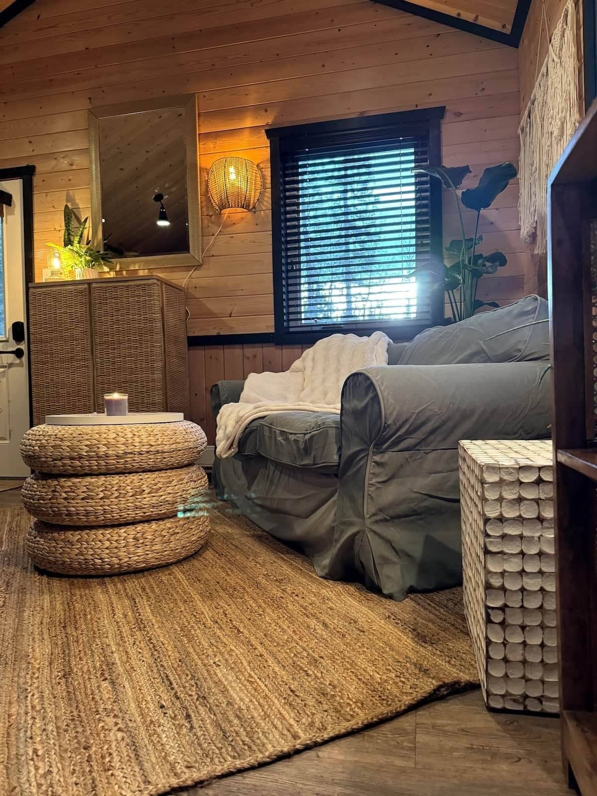A cozy room with a sofa, a woven rug, and a stack of firewood.