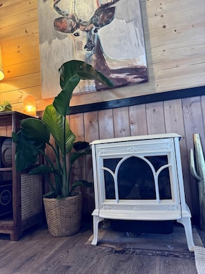 A room with a white fireplace, a wooden wall, and a painting of deer above it. - Two Pine Cabin (Rocky View County)