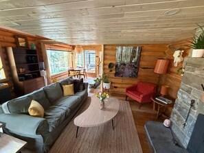 A cozy cabin interior with a sofa, a red chair, a coffee table, and a fireplace.