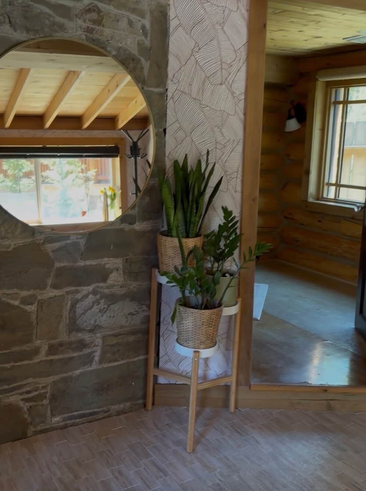 A room with a stone wall, a wooden ceiling, a window, and a plant stand with potted plants.