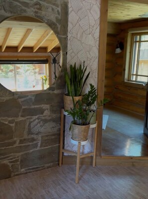 A room with a stone wall, a wooden ceiling, a window, and a plant stand with potted plants.