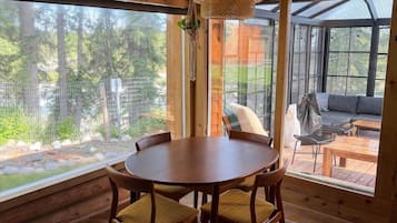A wooden interior with a round table and chairs, large windows, and a hanging light fixture.