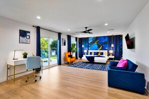 Un dormitorio moderno con cama, escritorio, silla y televisor.