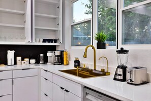 A modern kitchen with white cabinetry, a gold faucet, a Bosch dishwasher, and a coffee machine. - Chic Modern Vacation home in the heart of Dallas where comfort meets Luxury (Dallas)