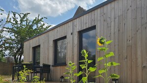 A wooden building with large windows, a deck, and a garden with plants and a sunflower. - “La Tiny de Miss Purple” with Terrace and Private Garden (Chantelle)
