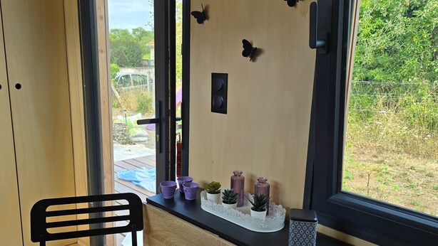 A room with a wooden desk, two chairs, a window with a view of greenery, and decorative butterfly wall art. - “La Tiny de Miss Purple” with Terrace and Private Garden (Chantelle)
