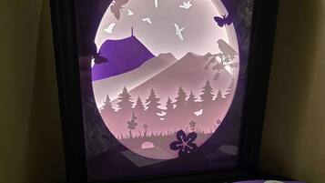 A framed artwork with a circular design featuring mountains, trees, and flying birds.