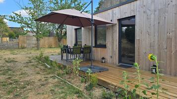 Une terrasse en bois avec une table et des chaises, un grand parasol et un jardin avec des plantes.