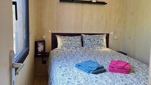 A bedroom with a wooden ceiling fan, a bed with patterned bedding, a nightstand with a lamp, and a window with curtains. - “La Tiny de Miss Purple” with Terrace and Private Garden (Chantelle)