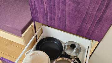 Un tiroir de cuisine dont l’intérieur est violet, contenant une casserole blanche, une poêle noire et une casserole en acier inoxydable avec un couvercle.