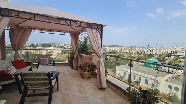 Ein Balkon mit überdachter Sitzecke, Pflanzgefäßen und Blick auf die Stadtlandschaft.