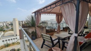 Ein Balkon mit Tisch und Stühlen, Blumentöpfen und Blick auf die Stadt.
