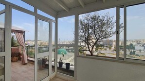 Ein Balkon mit Blick auf die Stadt, eine überdachte Sitzgelegenheit und Kübelpflanzen.
