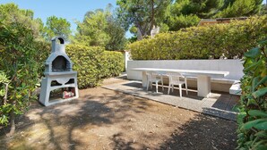 A barbecue grill, a white table with chairs, and a hedge in a garden setting. - Two-room Apartment with Veranda and Garden 100m from the Sea - Villaggio Sole e Mare (Rio)