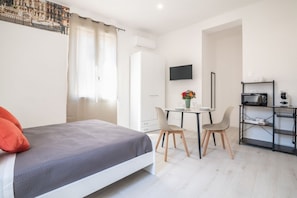 Un dormitorio con cama, escritorio, sillas, televisión y kitchenette.