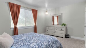 Quarto com cama, cômoda, espelho e janela com cortinas.