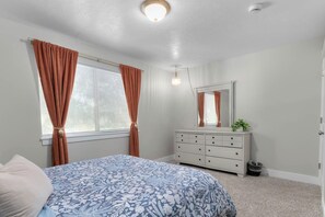 Ein Schlafzimmer mit Bett, Kommode, Spiegel und einem Fenster mit Vorhängen.