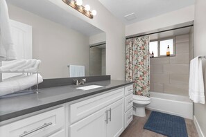 Ein modernes Badezimmer mit Waschtisch, Waschbecken, Spiegel und einer Duschkabine mit Blumenmuster.