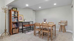 Uma área de refeições com mesa e cadeiras de madeira, uma estante e um abajur.