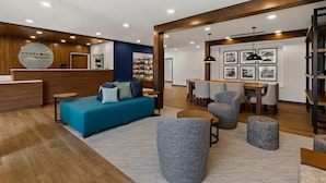 Un moderno vestíbulo de hotel con mostrador de recepción, un sofá azul, sillones grises, una zona de comedor y cuadros en la pared.