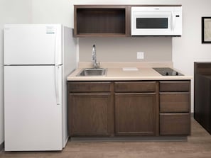 A compact kitchen with a refrigerator, microwave, sink, and wooden cabinets.