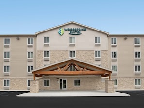 A hotel with a stone facade, multiple windows, and a central entrance with a wooden canopy. - Woodspring Suites Rock Hill Charlotte (Rock Hill)