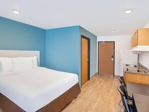 A hotel room with a bed, a desk, a chair, a kitchenette, and a door. - Woodspring Suites Rock Hill Charlotte (Rock Hill)