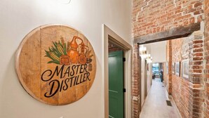 En träskylt med texten ”mästerdestillatör” och illustrationer av jordbruksrelaterade motiv, en grön dörr och en korridor med en tegelvägg.