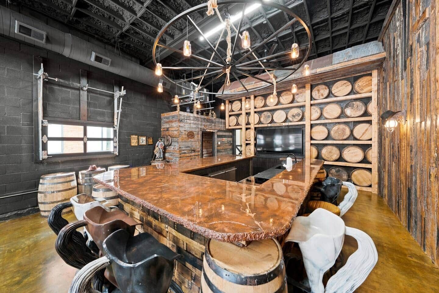 Un espace bar doté d’un grand comptoir en bois, de nombreux tabourets et d’un plafond avec des poutres apparentes et des luminaires suspendus.