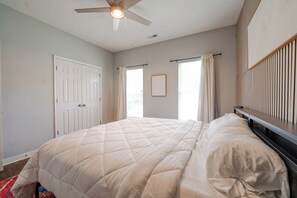 A bedroom with a bed, a ceiling fan, a window with curtains, and a door.