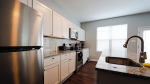 A modern kitchen with stainless steel appliances, white cabinetry, and a granite countertop.