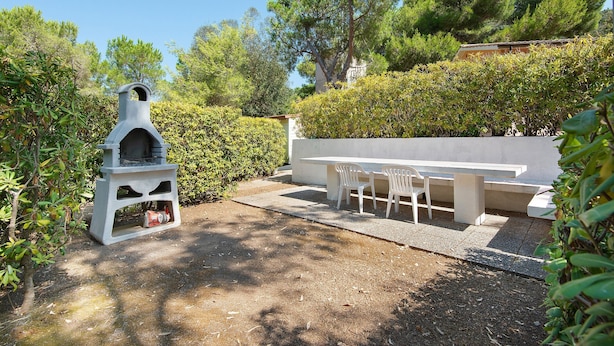 A barbecue grill, a white table with chairs, and a hedge in a garden setting. - Two-room Apartment with Veranda and Garden 100m from the Sea - Villaggio Sole e Mare (Rio)