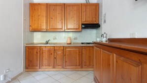 A kitchen with wooden cabinets, a gas stove, and a tiled backsplash. - Two-room Apartment with Veranda and Garden 100m from the Sea - Villaggio Sole e Mare (Rio)