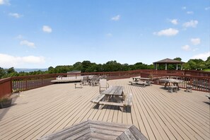 Eine Holzterrasse mit Picknicktischen und -stühlen, einem Pavillon und Blick auf die Landschaft.