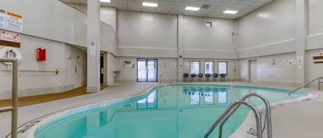 An indoor swimming pool with clear water, surrounded by a tiled floor and walls, and equipped with safety railings.
