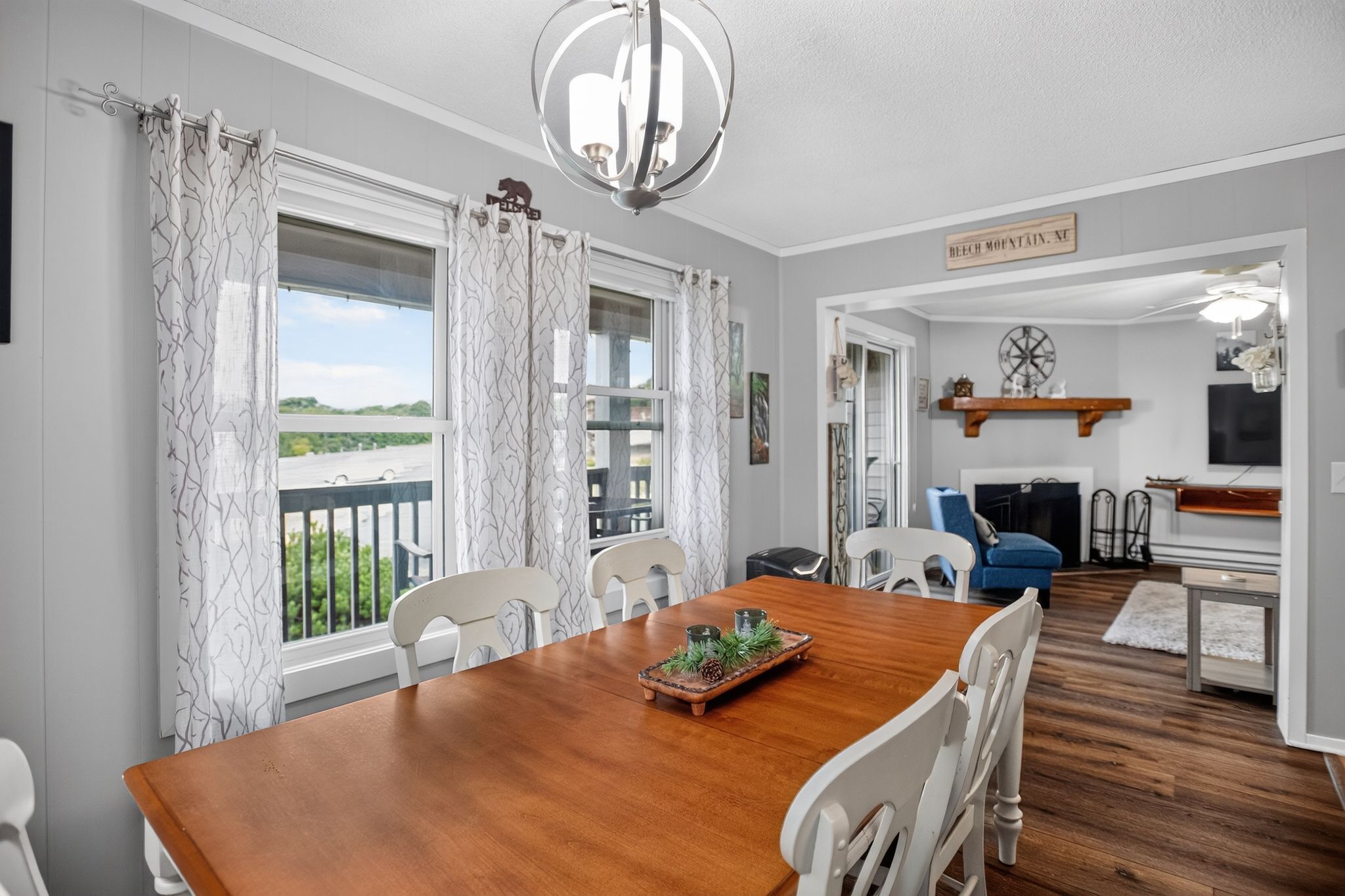 Un comedor con mesa de madera y sillas blancas, un candelabro y vistas al exterior.