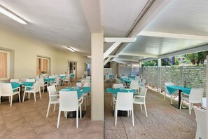 A restaurant with multiple tables and chairs, a tiled floor, and a ceiling with fluorescent lighting. - Two-room Apartment with Veranda and Garden 100m from the Sea - Villaggio Sole e Mare (Rio)