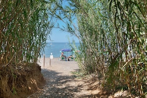 A pathway leading to a beach with umbrellas and a person sitting on a chair. - Two-room Apartment with Veranda and Garden 100m from the Sea - Villaggio Sole e Mare (Rio)