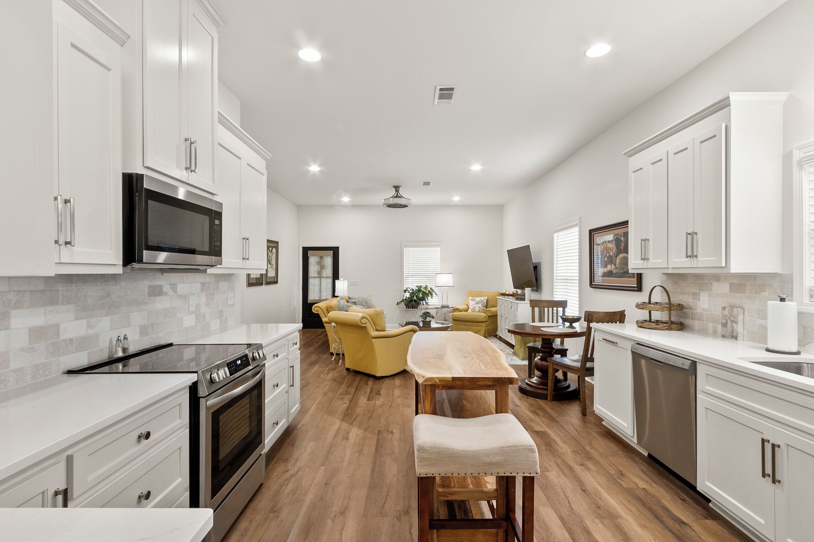 A modern kitchen with white cabinetry, a built-in microwave, and a dining area with a wooden table and yellow chairs.
