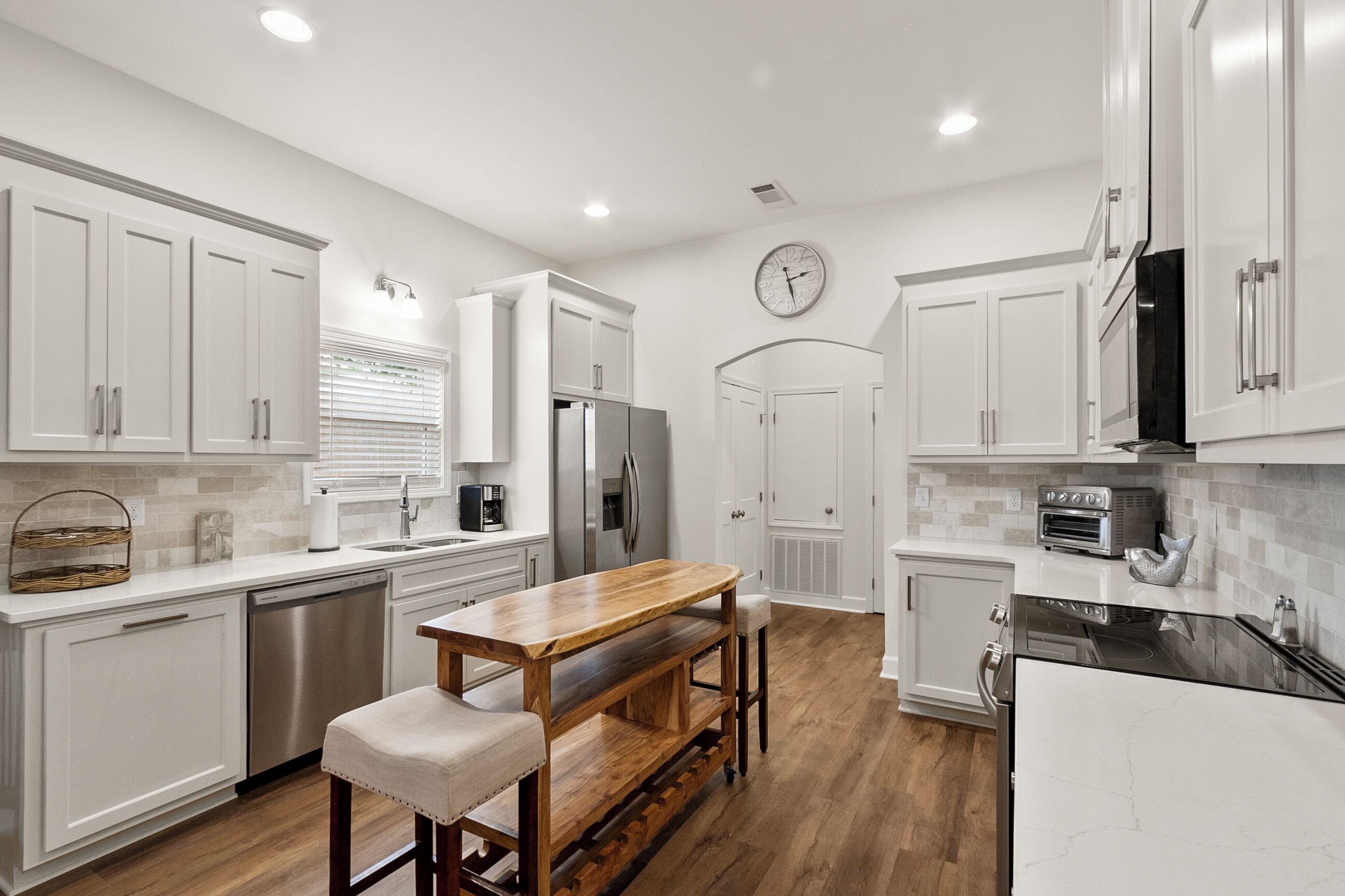 A modern kitchen with white cabinetry, stainless steel appliances, a wooden bench, and a clock on the wall.