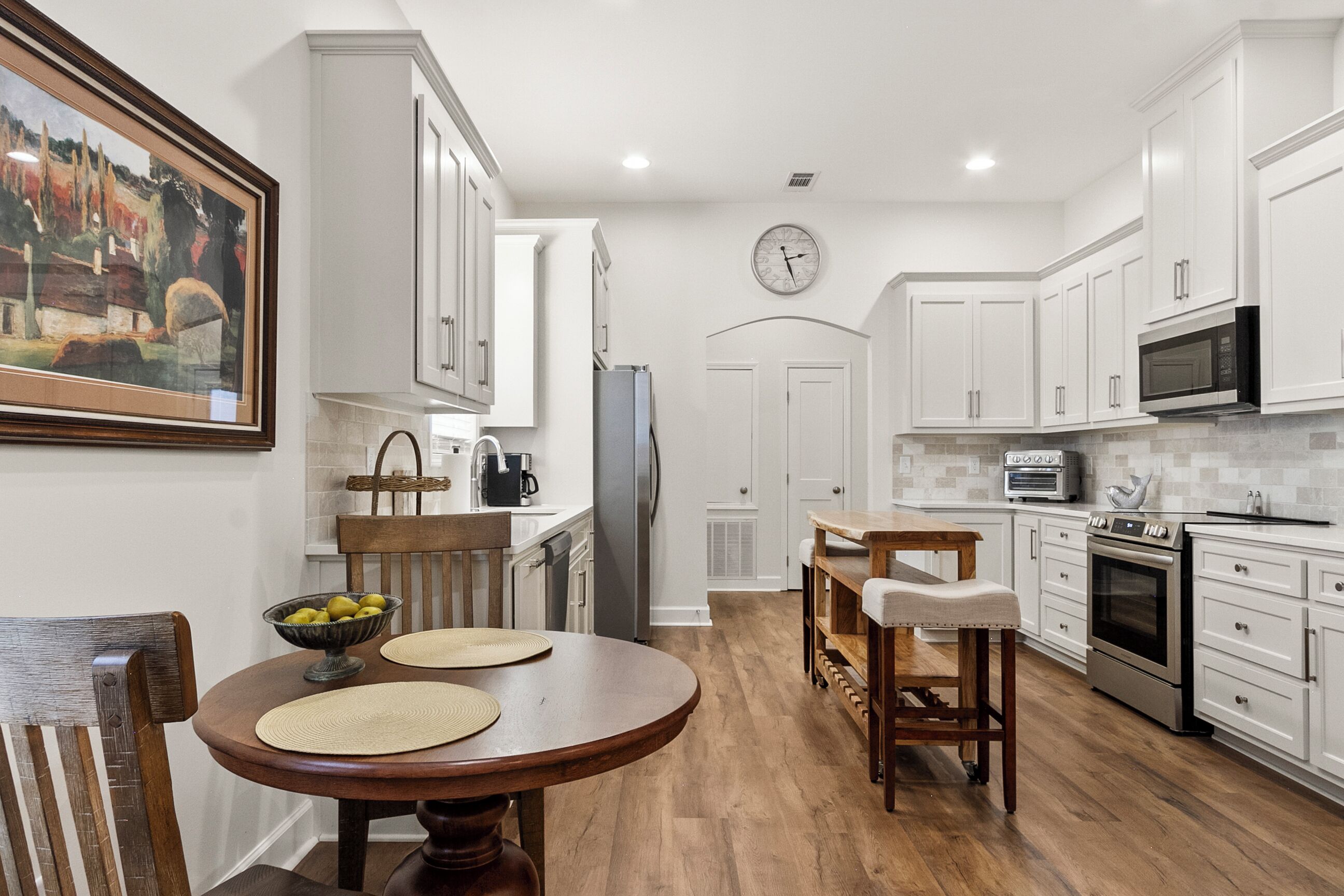 A modern kitchen with white cabinetry, a dining area with a wooden table and chairs, and a kitchen island.